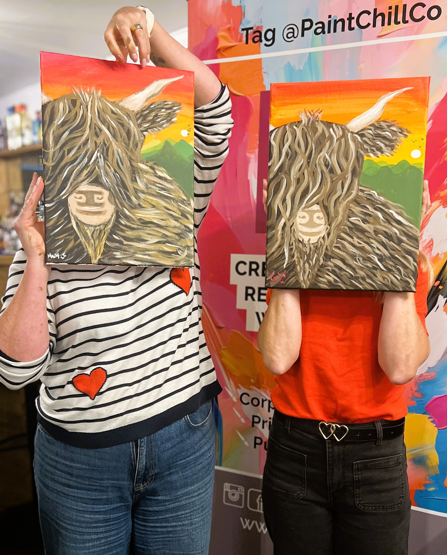 Happy customers holding their Highland cow paintings at a paint & sip event