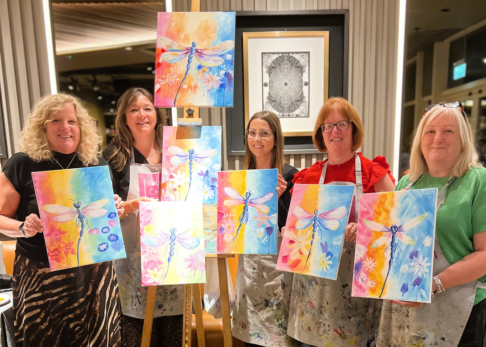 Group of customers showing their dragonfly paintings at a paint & sip event
